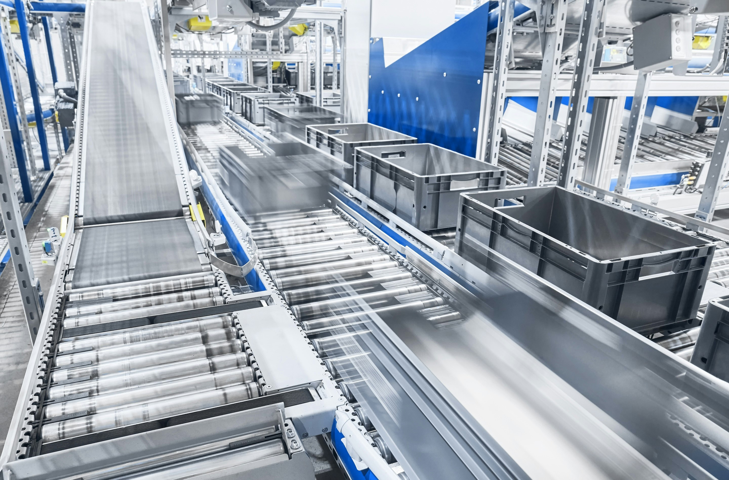 Silver chrome conveyor rollers, black conveyor belts, and cartons moving on them.